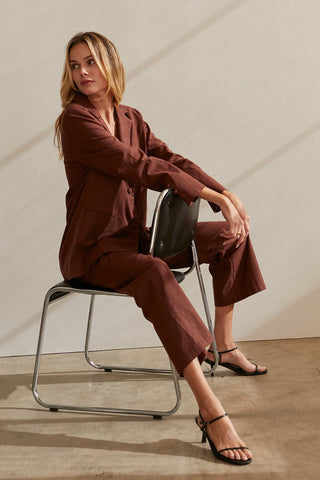 a model sitting down in a brown blazer and pants set