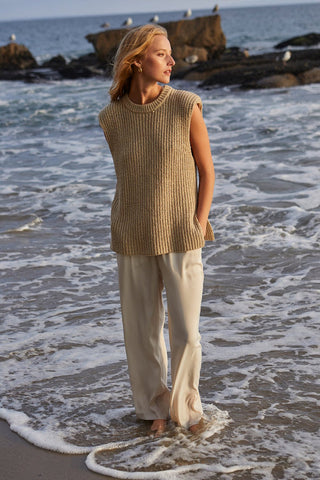 a model wading in the ocean in a beige sleeveless sweater and cream pants