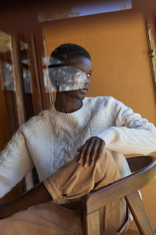 a woman looking through glass wearing a white knit sweater