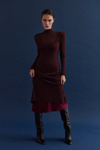 A woman wearing a sheer lurex knit mock neck maxi dress with long sleeves. 