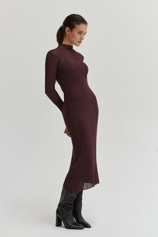 A woman wearing a sheer lurex knit mock neck maxi dress with long sleeves. 