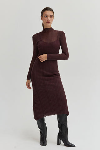 A woman wearing a sheer lurex knit mock neck maxi dress with long sleeves. 