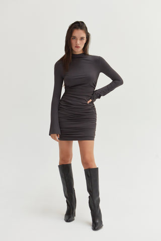 A woman wearing a mock neck ruched mini dress with long bell sleeves. 