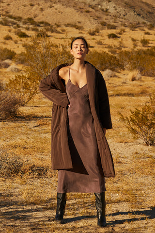 A woman wearing an oversized brown duvet puff coat with invisible side pockets and detachable self belt. 