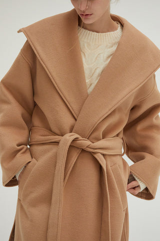 A woman wearing an oversized wrap style coat with a detachable self belt. 