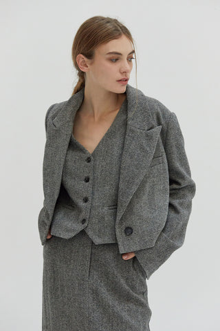 A woman wearing a cropped blazer with a two tone herringbone pattern. 
