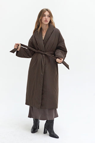 A woman wearing an oversized brown duvet puff coat with invisible side pockets and detachable self belt. 