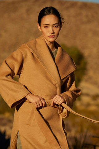 A woman wearing an oversized wrap style coat with a detachable self belt. 