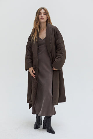 A woman wearing an oversized brown duvet puff coat with invisible side pockets and detachable self belt. 