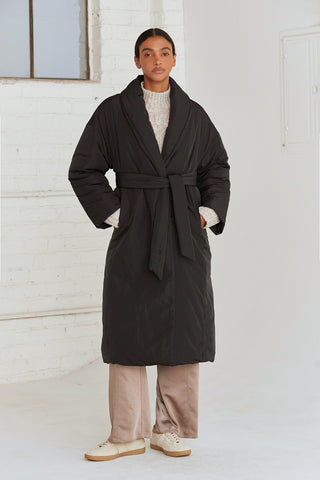 A woman wearing an oversized black duvet puff coat with invisible side pockets and detachable self belt. 