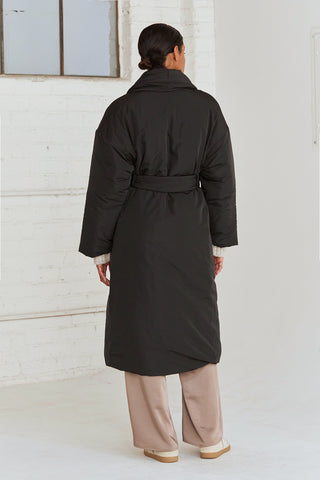 A woman wearing an oversized black duvet puff coat with invisible side pockets and detachable self belt. 