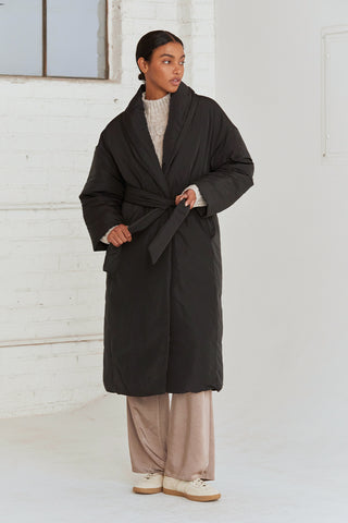 A woman wearing an oversized black duvet puff coat with invisible side pockets and detachable self belt. 