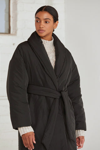 A woman wearing an oversized black duvet puff coat with invisible side pockets and detachable self belt. 