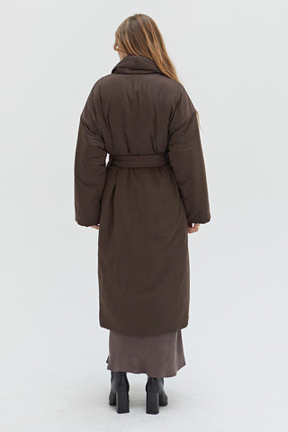 A woman wearing an oversized brown duvet puff coat with invisible side pockets and detachable self belt. 