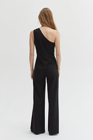 A woman wearing a black knit jumpsuit with a cut out detail at the shoulder.