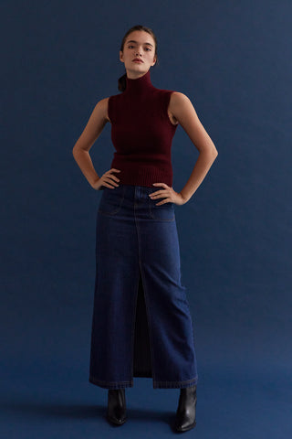 A woman wearing a high waisted denim maxi skirt with front center slit. 