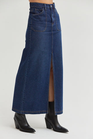 A woman wearing a high waisted denim maxi skirt with front center slit. 