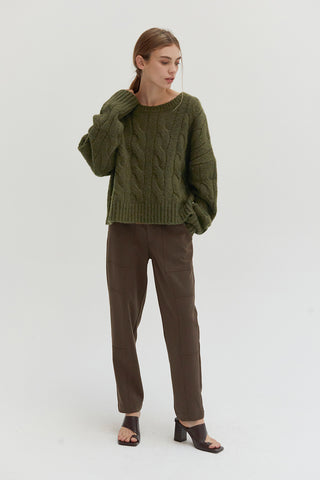 A woman wearing an olive chunky cable knit sweater.