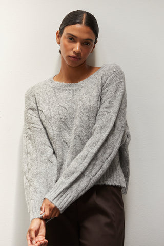 A woman wearing a heather grey chunky cable knit sweater.