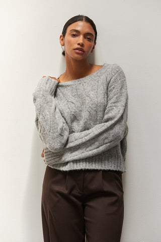 A woman wearing a heather grey chunky cable knit sweater.