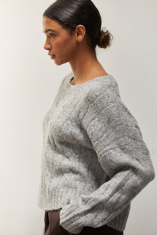 A woman wearing a heather grey chunky cable knit sweater.