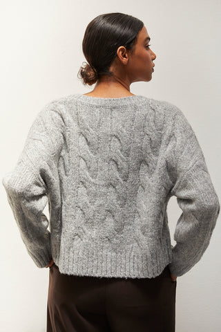 A woman wearing a heather grey chunky cable knit sweater.