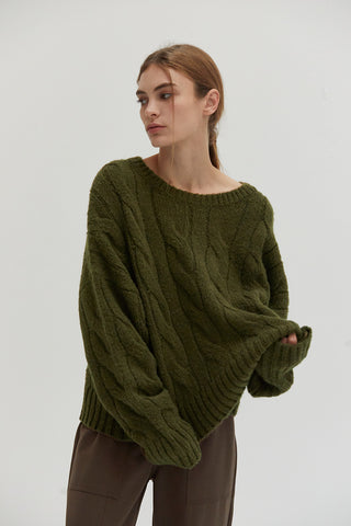 A woman wearing an olive chunky cable knit sweater.