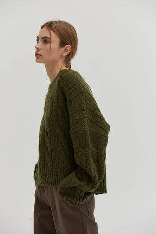 A woman wearing an olive chunky cable knit sweater.