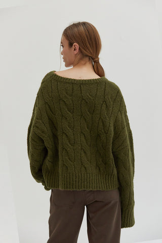 A woman wearing an olive chunky cable knit sweater.