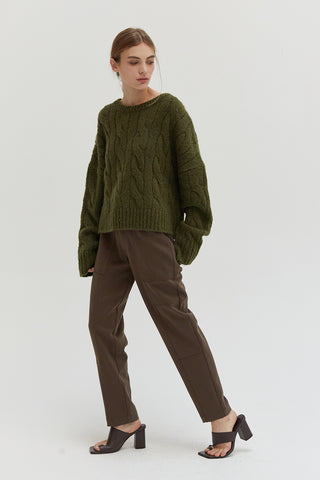 A woman wearing an olive chunky cable knit sweater.