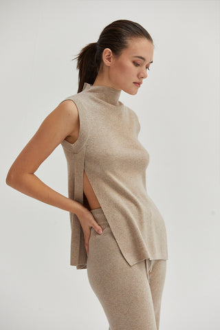 A woman wearing a mock neck sleeveless sweater top with side slit.