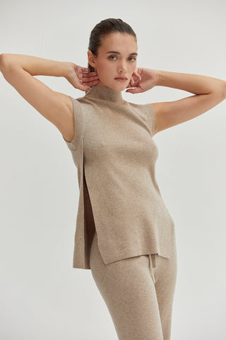 A woman wearing a mock neck sleeveless sweater top with side slit.