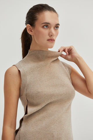 A woman wearing a mock neck sleeveless sweater top with side slit.