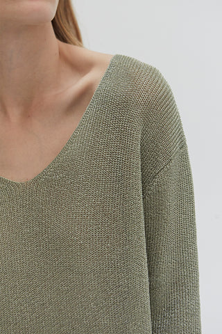 A woman wearing a green shimmer sweater knit top.