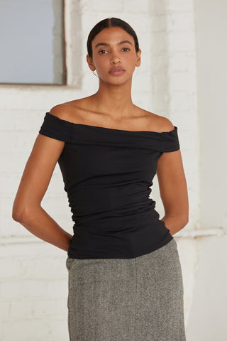 A woman wearing an off shoulder top with ruching at the sides. 