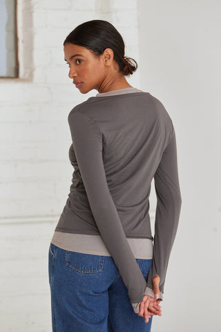 A woman wearing a dual layered long sleeve top with thumbholes. 