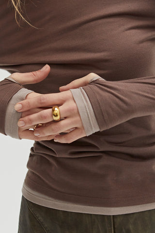 A woman wearing a dual layered long sleeve top with thumbholes. 