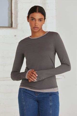 A woman wearing a dual layered long sleeve top with thumbholes. 