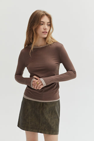 A woman wearing a dual layered long sleeve top with thumbholes. 