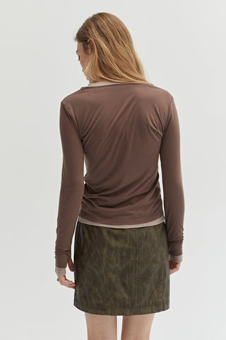 A woman wearing a dual layered long sleeve top with thumbholes. 