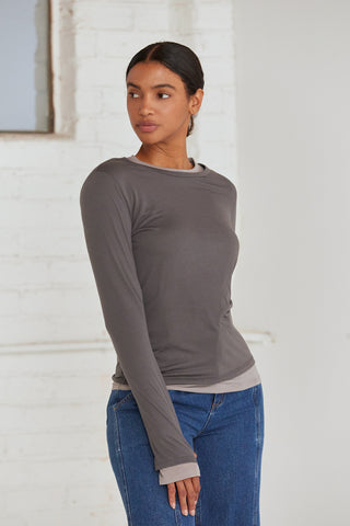 A woman wearing a dual layered long sleeve top with thumbholes. 