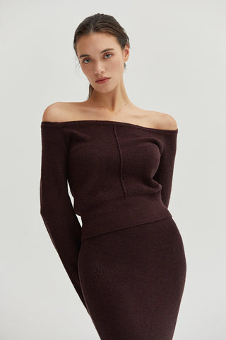 A woman wearing an off shoulder knit top and midi skirt two-piece sweater set.