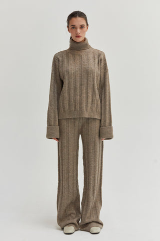 A woman wearing a ribbed sweater set with turtleneck top and pull on pants. 