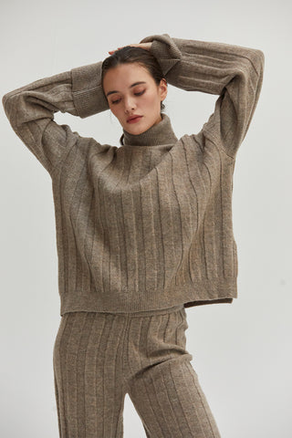 A woman wearing a ribbed sweater set with turtleneck top and pull on pants. 