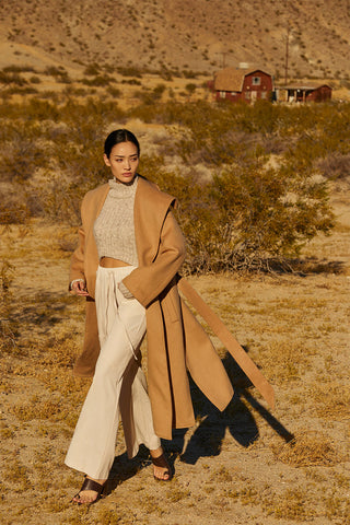 a model in a brown wool shawl coat and beige pants