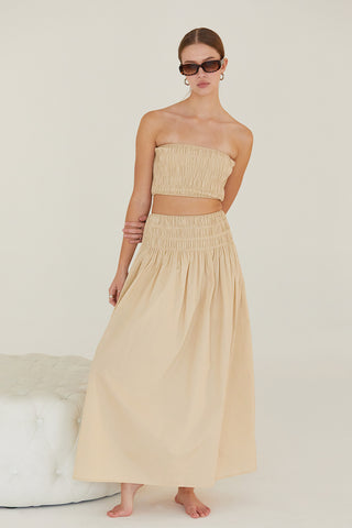 A woman wearing a beige all-over smoked tube top and maxi skirt two piece set.