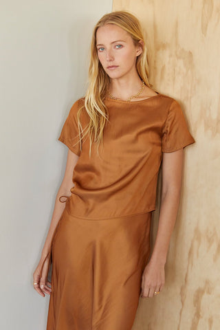 A model wearing a brown short sleeve satin blouse with tunnel ruching detail on one side.
